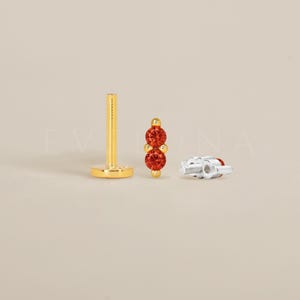Peut inclure: Bijou de corps en or avec deux pierres précieuses rouges. Le bijou est de style barre avec une extrémité à vis.