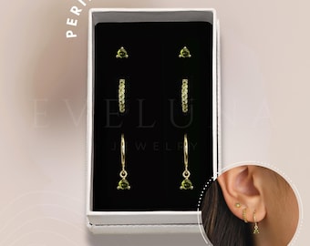 May include: A set of three gold earrings with peridot stones. The earrings are in a white box with the words "PERIDOT" and "EVLUA JEWELRY" printed on it.