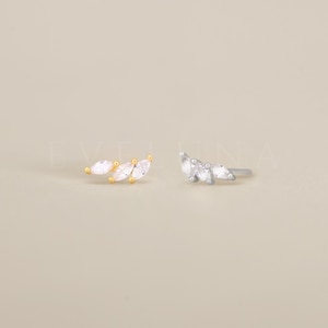 May include: Two pairs of earrings featuring a row of three marquise-shaped clear stones. The earrings are available in gold and silver.