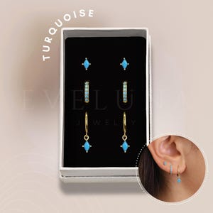 Può includere: Un set di orecchini turchesi in una scatola bianca. Il set include due paia di piccoli orecchini a bottone, un paio di piccoli orecchini a cerchio e un paio di orecchini pendenti. Gli orecchini sono tutti dorati e hanno pietre turchesi.