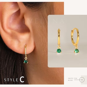 May include: Gold-colored hoop earrings with a small, dangling emerald-green gemstone. The earrings are shown on a person's ear and also displayed separately. The text "EVELUNA JEWELRY" is visible in the background. The style is labeled "STYLE C".