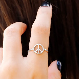 May include: A silver peace sign ring on a finger.