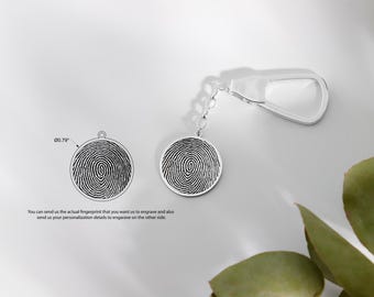 May include: Silver keychain with a round charm featuring a fingerprint design. The charm is attached to a silver chain and a silver loop. The text "You can send us the actual fingerprint that you want us to engrave and also send us your personalization details to engrave on the other side." is visible below the charm.