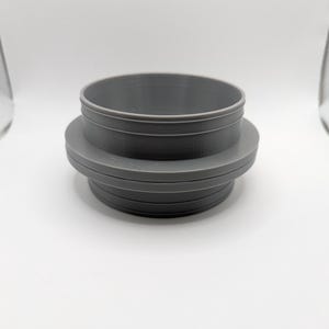 May include: A gray plastic adapter with a smooth, rounded surface and a slightly raised lip around the top edge.