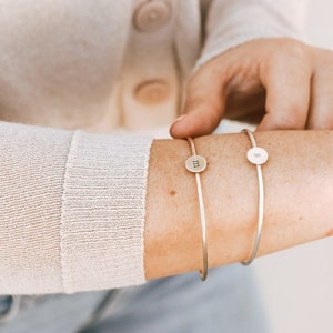Puede incluir: Dos pulseras de plata con dijes de iniciales. La pulsera de la izquierda tiene la letra "M" en el dije y la pulsera de la derecha tiene la letra "S" en el dije.