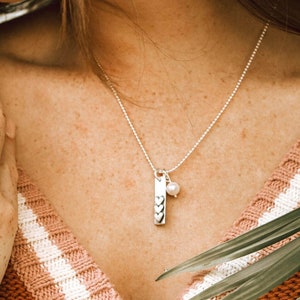 May include: A silver necklace with a charm that has three hearts and a small pearl hanging from it.