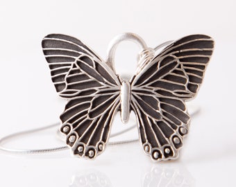 May include: A silver butterfly pendant necklace with a detailed design. The butterfly is suspended from a delicate silver chain.