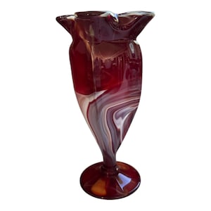 May include: A red and white swirled glass vase with a wide mouth and a flared base.
