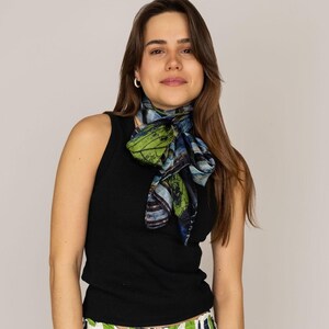 Könnte beinhalten: Eine Frau trägt ein schwarzes Tanktop, eine weiße Hose mit einem geometrischen Muster in Grün und Blau und einen grün-blau-braunen gemusterten Schal, der um ihren Hals gebunden ist.