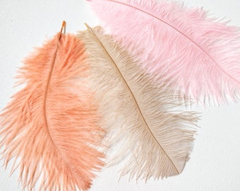 Puede incluir: Tres plumas de avestruz en diferentes tonos de rosa y melocotón. Las plumas son suaves y esponjosas, con un aspecto natural y elegante.