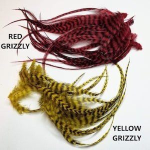 May include: Two bundles of feathers, one red and one yellow, with black stripes. The red bundle is labeled "RED GRIZZLY" and the yellow bundle is labeled "YELLOW GRIZZLY".