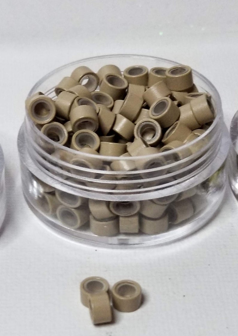 Puede incluir: Un recipiente de pl&aacute;stico transparente lleno de peque&ntilde;os microanillos marrones claros para extensiones de cabello.