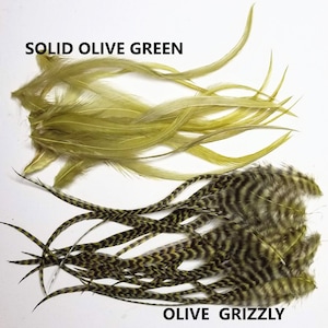 May include: Two bundles of feathers, one solid olive green and one olive grizzly. The olive grizzly feathers have a black and olive green chevron pattern.