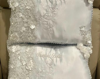 May include: Two white satin pillow covers with lace trim and embroidered doves. The pillows are decorated with white flowers and the text "Nuestra Boda" which translates to "Our Wedding" in English.