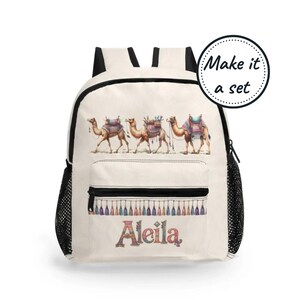 May include: A cream-colored backpack featuring a graphic of three camels with colorful saddles, a row of hanging tassels, and the name Aleila printed in a decorative font. A circular badge in the top right corner displays the text Make it a set.