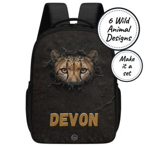 Op de afbeelding: Zwarte rugzak met een cheeta-ontwerp en de naam "Devon" in gouden letters. Het gezicht van de cheeta lijkt uit een getextureerde achtergrond te komen. Bevat de tekst "6 Wild Animal Designs" en "Make it a set".