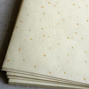May include: A stack of cream-coloured paper with flecks of gold throughout.