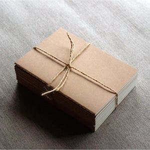 May include: A stack of brown cardstock paper is tied together with twine. The paper is blank and ready for writing or crafting.