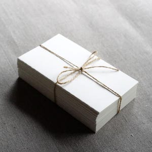 May include: A stack of blank white cards tied together with twine. The cards are arranged in a neat pile and the twine is tied in a simple bow.