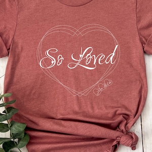 May include: A maroon t-shirt with a white heart design and the text "So Loved" inside the heart.