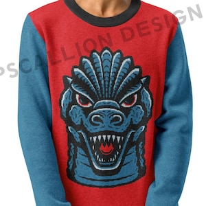 Può includere: Una felpa rossa con maniche blu e colletto nero. La parte anteriore presenta una grafica di mostro blu con occhi rossi e denti affilati. La felpa è indossata da una persona.