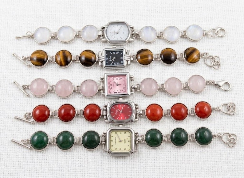 May include: Five silver-toned bracelets with gemstone accents and watch faces. The gemstones include moonstone, tiger's eye, rose quartz, red jasper, and green malachite. The watch faces have various shapes and colors.