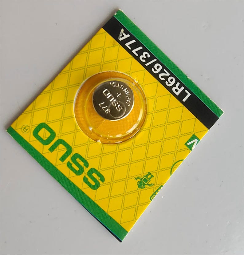 May include: A small, silver 377 battery cell is visible through a clear plastic window on a yellow and green package. The package has a diamond pattern and the brand name "onss" is printed on the front. The package also has the text "LR626/377A".
