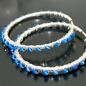 May include: A pair of silver hoop earrings with blue gemstone accents. The hoops are made of thin wire and are adorned with small, round blue stones.