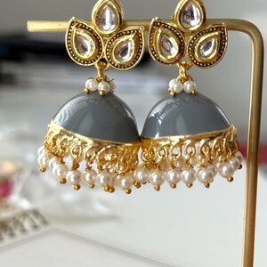 May include: Gray and gold earrings with pearl accents. The earrings feature a round, gray base with a gold rim and a cluster of three gold leaves with clear stones at the top.