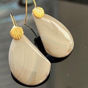 May include: A pair of gray agate earrings with gold shell accents. The earrings are teardrop shaped and have a smooth, polished finish.