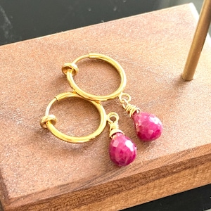 May include: A pair of gold hoop earrings with dangling pink gemstone drops.