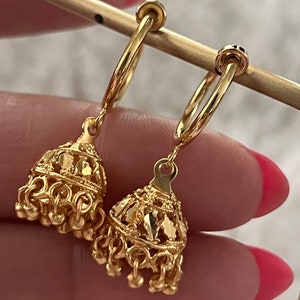 May include: A pair of gold hoop earrings with a dangling charm. The charms are intricate and feature a filigree design.