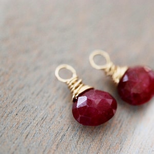 以下が含まれることがあります： 涙の形をした赤い宝石のイヤリングが2つ、金色のワイヤーで包まれています。