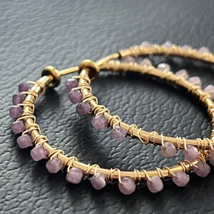 May include: Gold hoop earrings with a row of small purple gemstones around the edge.