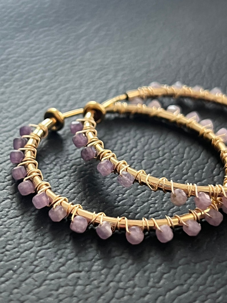 May include: Gold hoop earrings with a row of small purple gemstones around the edge.
