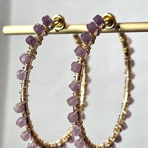 May include: Gold hoop earrings with a delicate wire design and small purple gemstones. The earrings are approximately 2 inches in diameter.