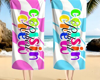 May include: Two beach towels, one pink and one blue, are held up against a beach backdrop. Each towel has a white background with a colorful, abstract design and the text "Robert Cousin" in a playful font.