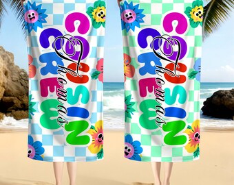 May include: Two beach towels with a colorful floral and checkerboard pattern. The towels feature the name "Thomas" in a whimsical font. The towels are held up on a sandy beach with palm trees in the background.