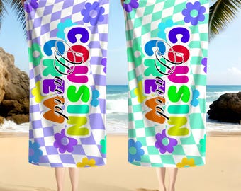 May include: Two beach towels with a checkered pattern and the text "Cousin David". One towel is purple and white, the other is teal and white. Both have colorful flower accents.