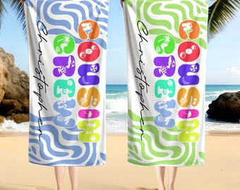 May include: Two beach towels, one blue and one green, are held up against a beach backdrop. Each towel has a white background with a colorful design and the name "Christopher" in script. The towels feature a colorful design with the word "SUMMER" in large, bubble letters.