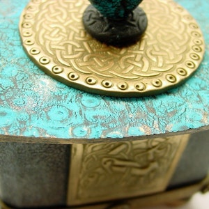 May include: A teal blue wooden box with a gold metal Celtic knot design lid. The lid has a raised, circular design with a black knob.