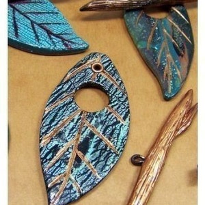 May include: A teal blue and copper leaf pendant with a hole in the center. The leaf has a textured surface and gold accents. The pendant is handmade and unique.