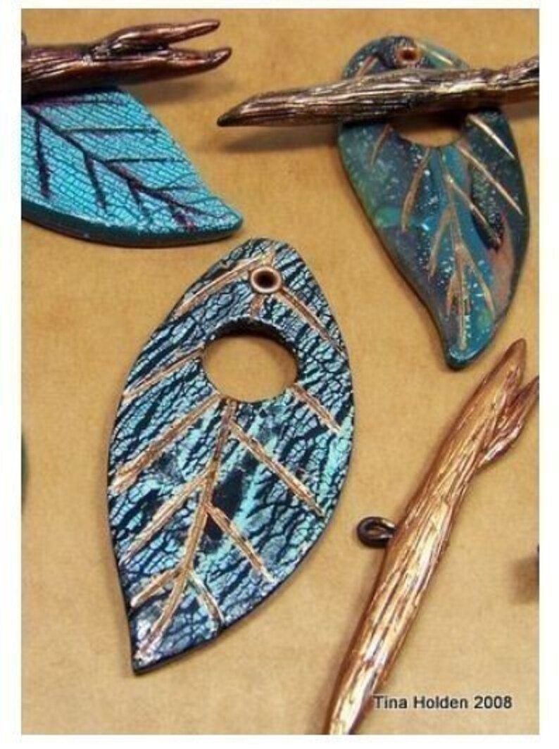 May include: A teal blue and copper leaf pendant with a hole in the center. The leaf has a textured surface and gold accents. The pendant is handmade and unique.