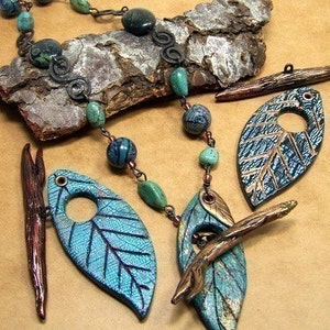 May include: A turquoise and gold leaf necklace with a copper branch accent. The necklace features a beaded chain with turquoise and black beads. The leaves are made of polymer clay and have a textured surface. The branch is made of copper wire and has a rustic finish.
