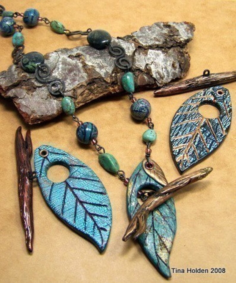 May include: A turquoise and gold leaf necklace with a copper branch accent. The necklace features a beaded chain with turquoise and black beads. The leaves are made of polymer clay and have a textured surface. The branch is made of copper wire and has a rustic finish.