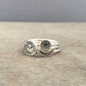 May include: A set of three silver rings with celestial designs. The rings feature a sun, a moon, and a star.