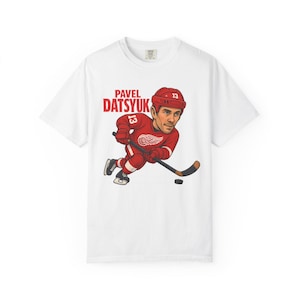 Könnte beinhalten: Weißes T-Shirt mit einer Cartoon-Illustration von Pavel Datsyuk in einem roten Hockey-Trikot. Der Text "PAVEL DATSYUK" befindet sich über der Illustration. Der Spieler hält einen Hockeyschläger und einen Puck.