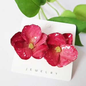 May include: A pair of pink flower earrings with gold centres. The earrings are on a white card with the word "JEWELLERY" printed on it.