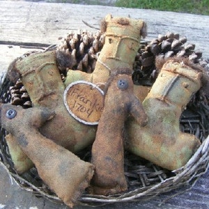 May include: A rustic basket filled with several handmade fabric dolls and pinecones. The dolls are in shades of brown and green, with button eyes and a tag that reads "Frankie 1704". The basket is made of woven twigs, creating a charming, country-style aesthetic.