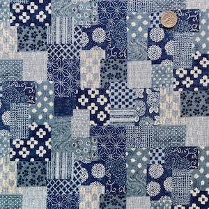 May include: A patchwork fabric with a variety of blue and white patterns. The design includes floral, geometric, and dotted motifs. A quarter coin is visible for scale, showing the fabric's texture and detail.